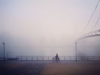 Man on bridge over river against sky during foggy weather