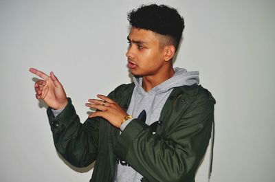 Young man pointing against white wall