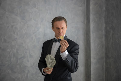 Businessman holding money while standing against wall