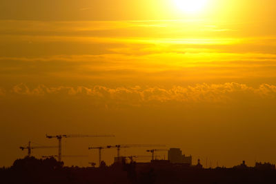 Silhouette cranes against sky during sunset
