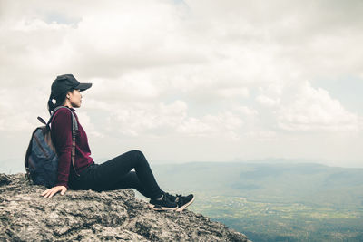 Man sitting on rock looking at mountain against sky
