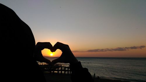 Silhouette of heart shape on beach at sunset
