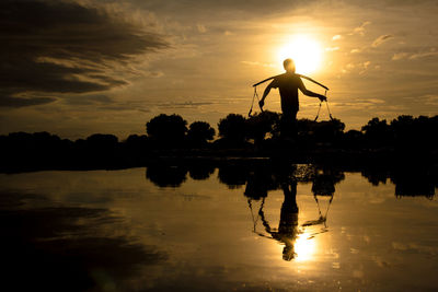 Silhouette men standing by lake against sky during sunset