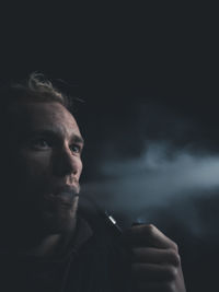 Close-up of young man smoking against black background