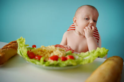 A child eats sausage with pasta and baguette