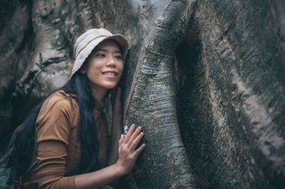 Portrait of smiling young woman standing on tree trunk