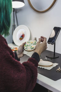 Young woman with dyed hair embroidering cloth at table in studio