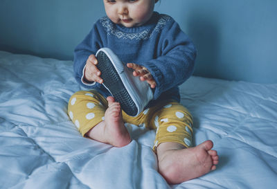 Playful cute girl holding shoe on bed