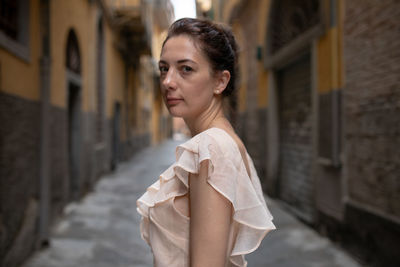 Portrait of woman standing at alley amidst buildings