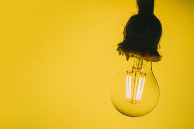 Close-up of light bulb hanging against yellow background