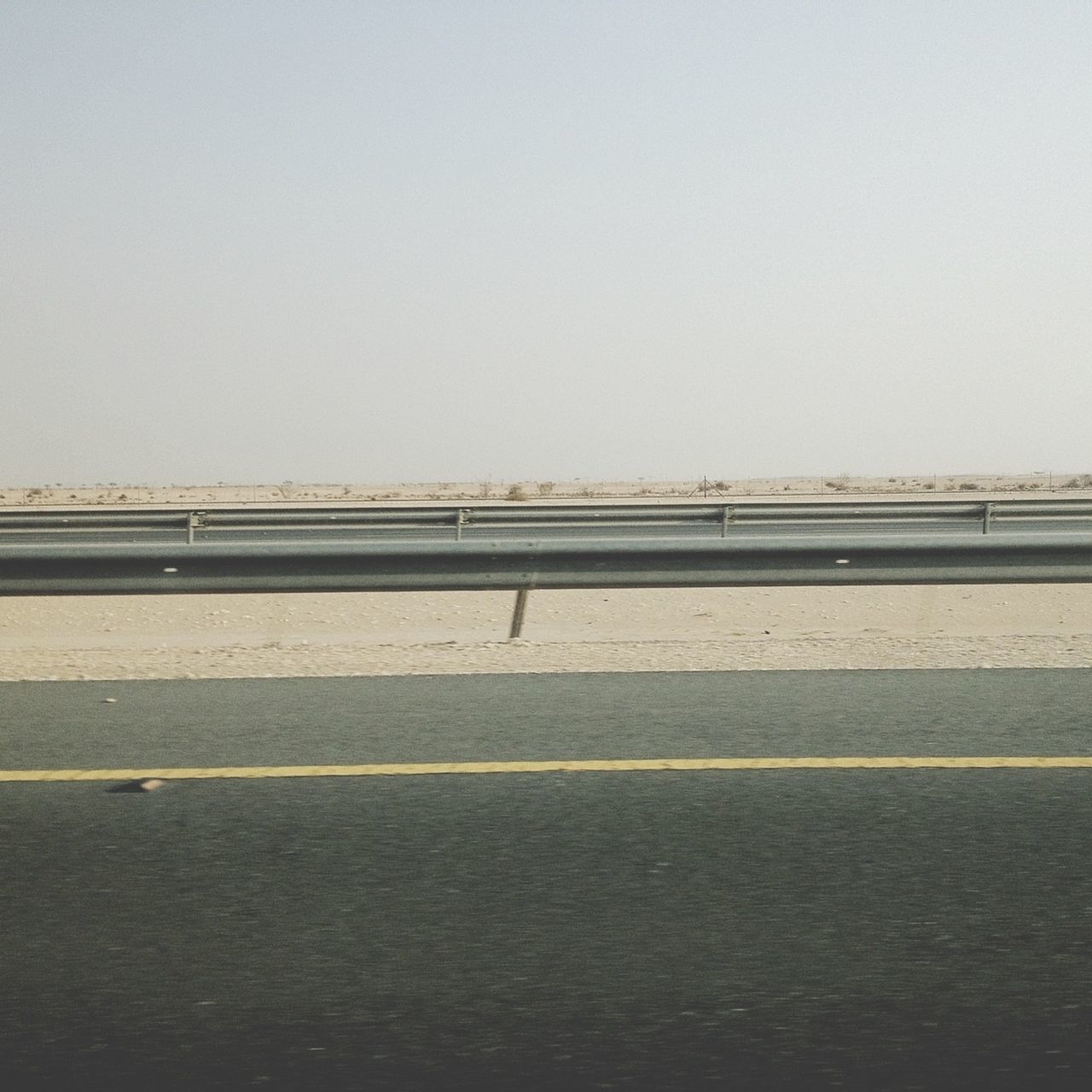 clear sky, copy space, architecture, built structure, building exterior, road, transportation, road marking, outdoors, street, day, railing, the way forward, city, no people, wall - building feature, sky, connection, empty, building