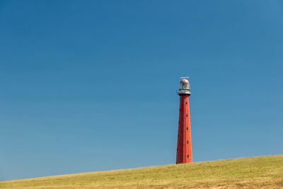 Lighthouse by sea against clear blue sky