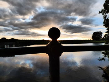 Silhouette boy looking at lake against sunset sky