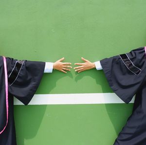 Midsection of students in graduation gowns standing against wall