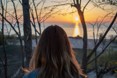 Rear view of young woman looking at sea against sky during sunset