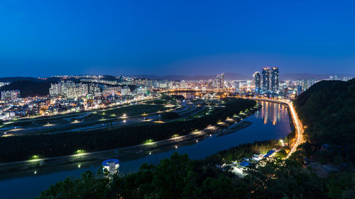 High angle view of illuminated city buildings against blue sky