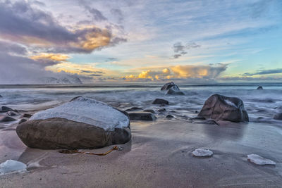 Rocks on beach against sky during sunset