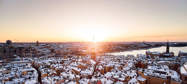 Snow covered buildings against sky during sunset