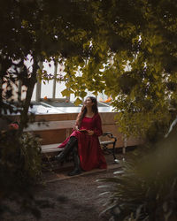 Rare view of woman sitting on the bench with a book in the red long dress, daydreaming