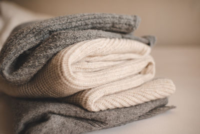 Stack of knitted wool textile sweaters clothes on white blanket in bed at home room close up. 