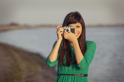 Portrait of young woman photographing while standing on beach