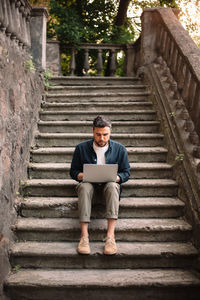 Man using laptop computer sitting on steps in city