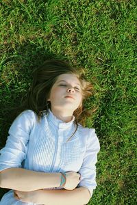 High angle view of young woman with closed eyes relaxing on grassy field