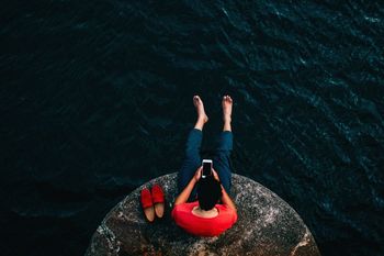 Man using mobile phone while sitting on rock at sea