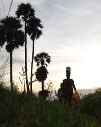 Man sitting by palm trees on field against sky