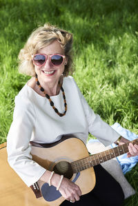 Smiling senior woman wearing sunglasses playing guitar in park