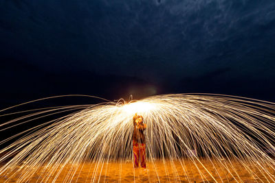 Womanwith wire wool standing on sand at night