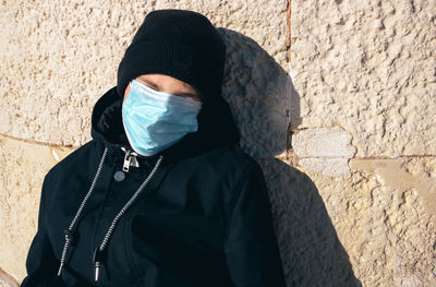 Portrait of teenager with a mask standing against wall