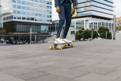 Spain, barcelona, legs of young businessman riding skateboard in the city