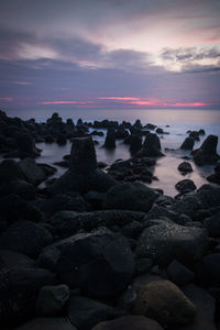 Rocks on beach against sky during sunset