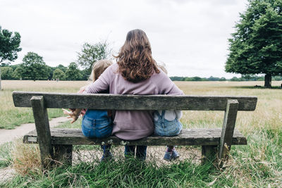 Mother sitting with arms around daughters on bench