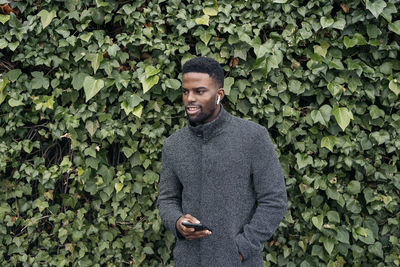 Young smiling man listening music against plants