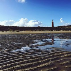 Lighthouse at beach against sky