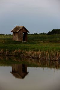 House on field by lake against sky