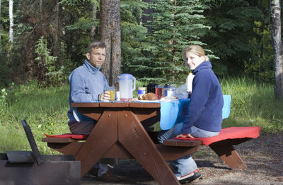 Portrait of father and daughter having food and drink on picnic table in forest