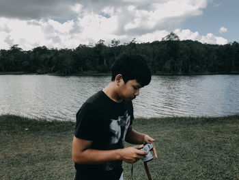 Man photographing while standing by lake against trees