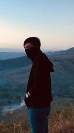 Side view of young man standing on mountain against sky