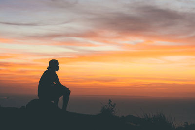 Silhouette man sitting on rock against sky during sunset