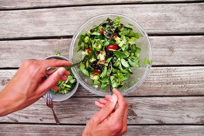 Directly above shot of hand mixing salad in bowl on table