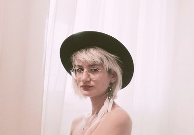 Portrait of young woman in hat against wall