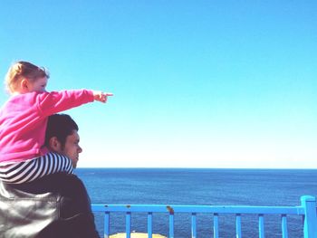 Woman standing by sea against clear blue sky