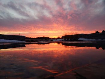 Scenic view of lake against dramatic sky during sunset