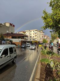 Cars on road by buildings in city against sky