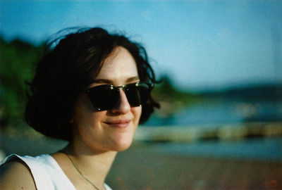 Portrait of smiling young woman wearing sunglasses against sky