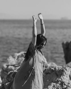 Young woman standing on rock formation against sky