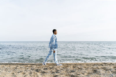 Young man wearing denim outfit walking against sea